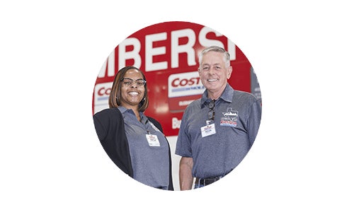 Two Costco employees (female and male) smiling and standing in front of Costco Membership sign