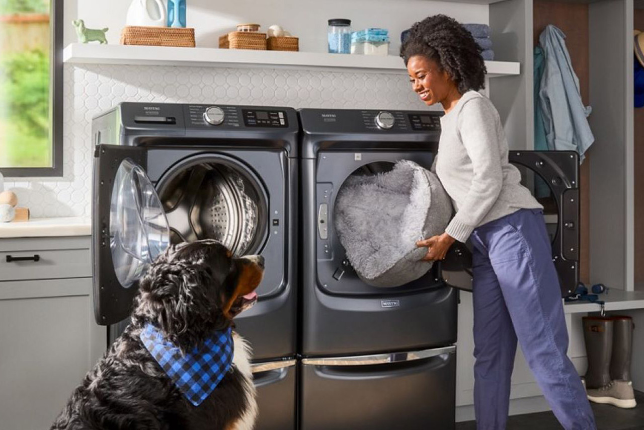 Woman looking at dog as she is loading laundry into a front load washer, which is next to a dryer