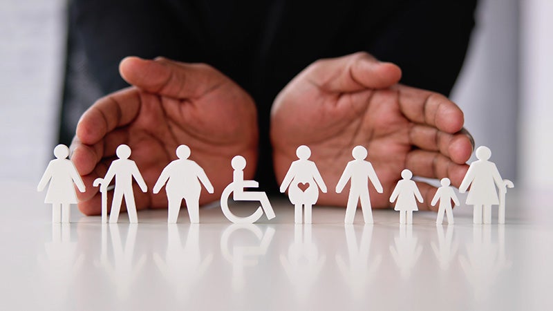 Hands displaying diverse and differently-abled paper figures representing inclusion and belonging