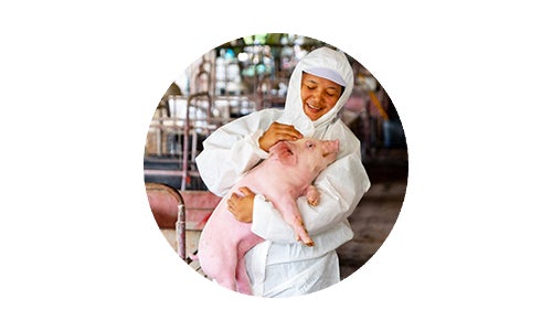 Woman in protective white suit cradling a pink piglet and smiling