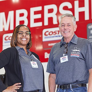 Female and male Costco employees in front of Costco Membership sign
