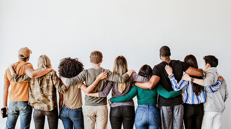 Line of diverse people with arms around shoulders facing away from camera
