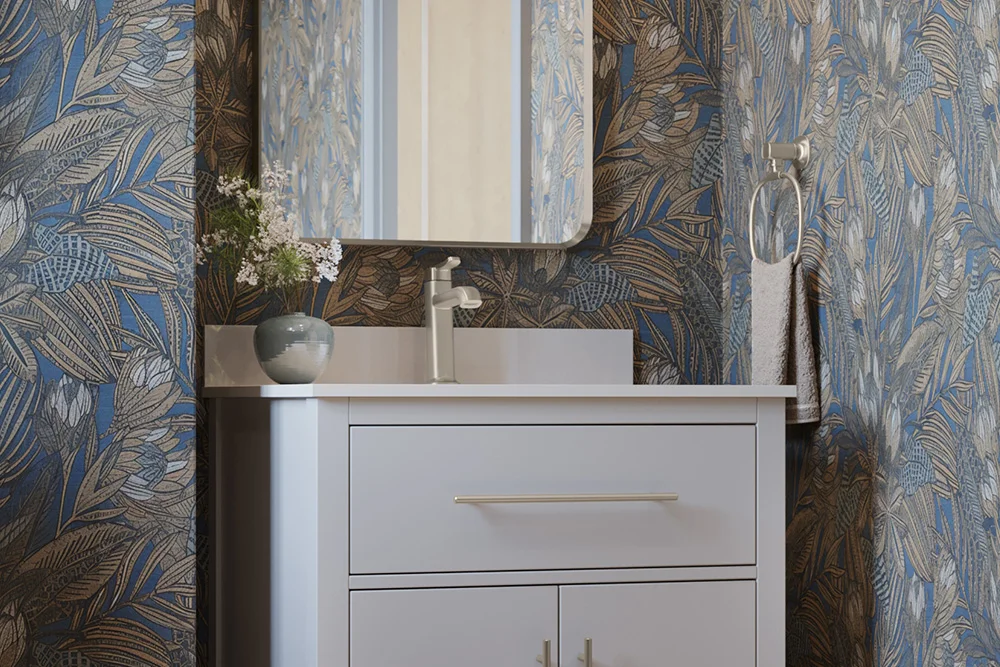 A white singular bathroom sink and cabinet with silver bathroom faucet and white countertop and cabinets. Surrounding are blue with gold flowered wallpaper.