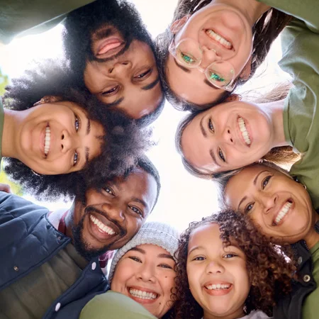 Inclusive circle of people leaning over camera and smiling